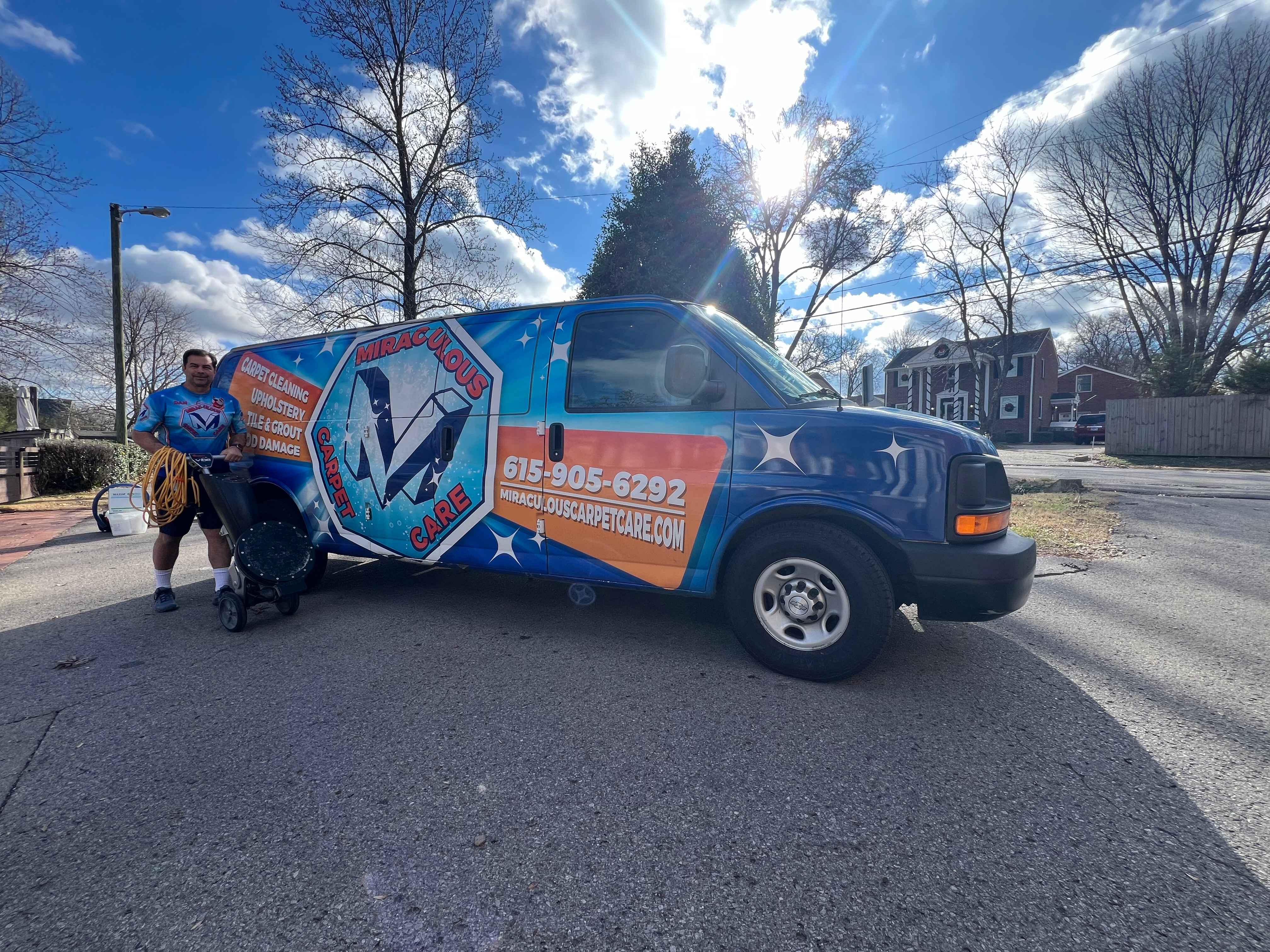 Miraculous Carpet Care technician smiling while pulling cleaning equipment beside the company's branded van under a bright Franklin, TN sky