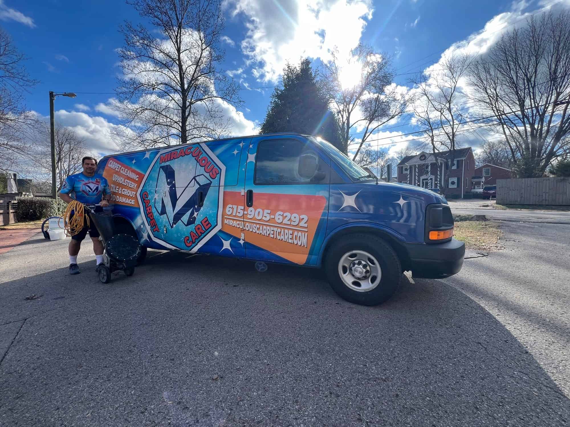 Miraculous Carpet Care technician smiling while pulling cleaning equipment beside the company's branded van under a bright Franklin, TN sky